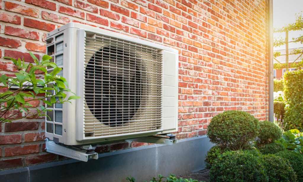 A heat pump unit hanging on a brick wall outside a home